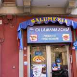Il negozio si affaccia sulla strada. Sulla porta a vetri sono affissi i manifesti della compagnia telefonica rumena e l�insegna blu con la scritta in italiano �salumeria� e il nome �Ca la mama acasa � prodotti tipici rumeni�